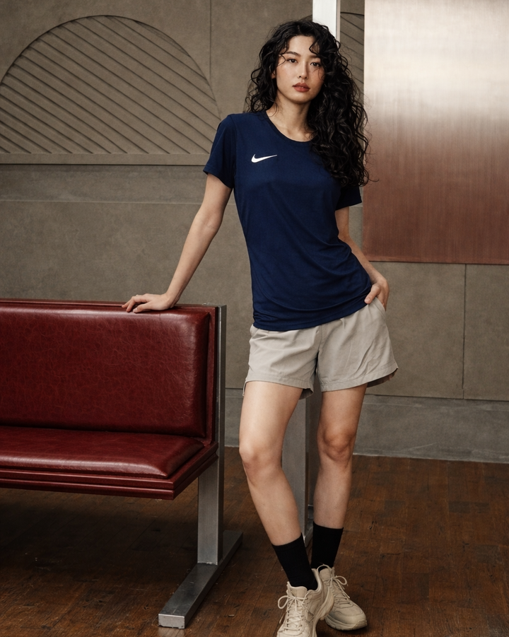 Woman wearing a navy blue Nike t-shirt and beige shorts standing in an indoor setting.