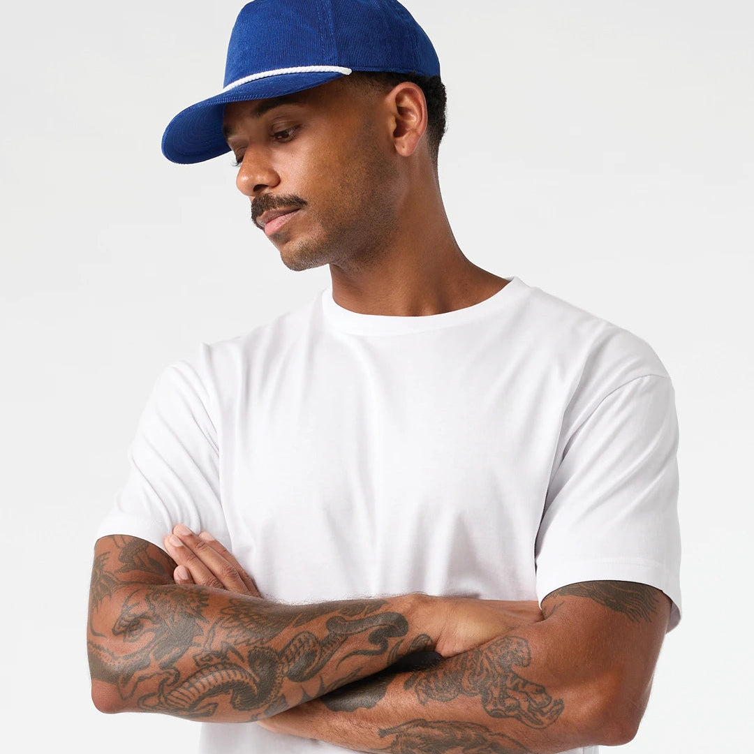 AS Colour white Staple Tee on male model side profile view with blue hat