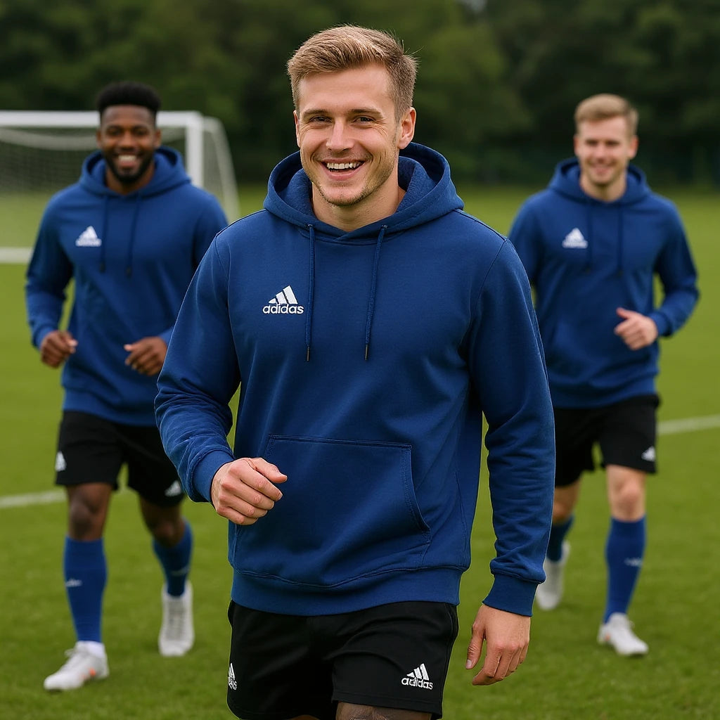 Man wearing a blue Adidas hoodie on a sports field with two other people in the background.