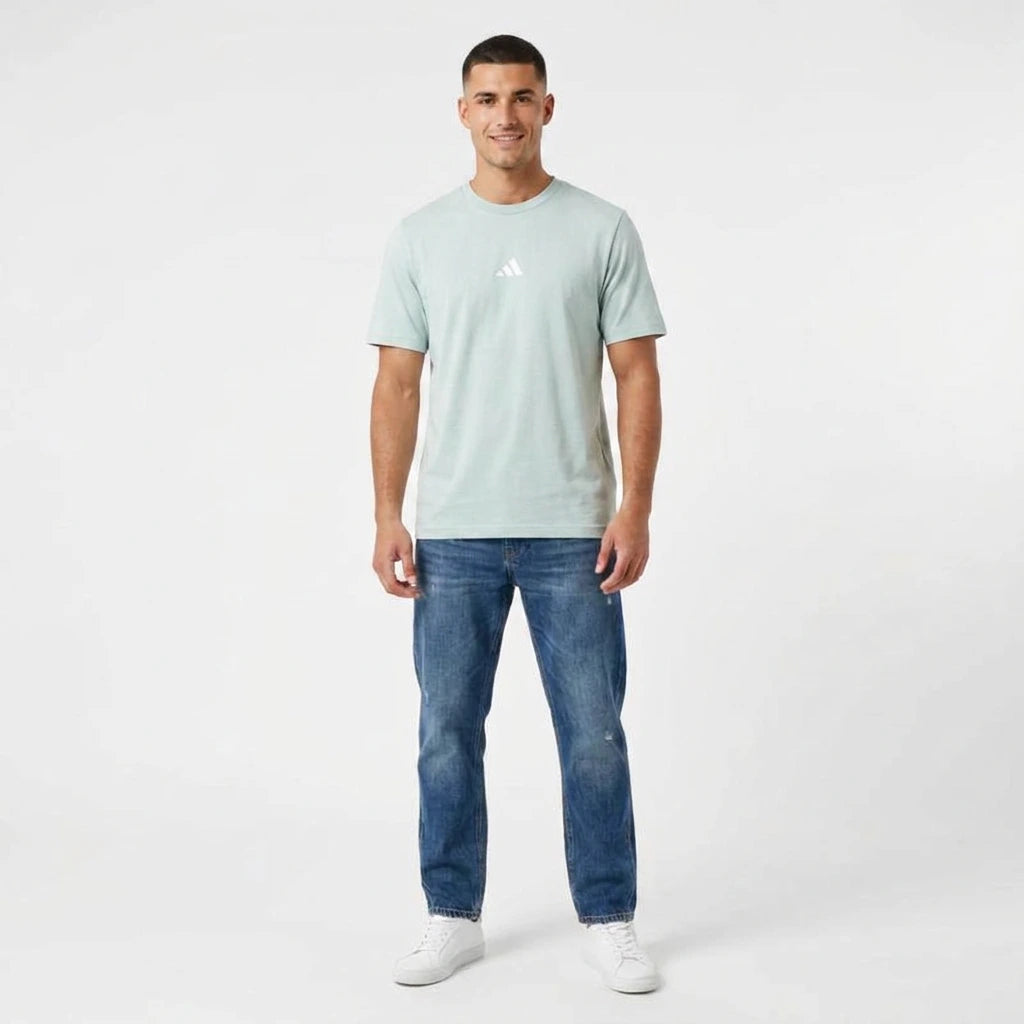 Man wearing a light blue t-shirt with a logo and blue jeans on a white background