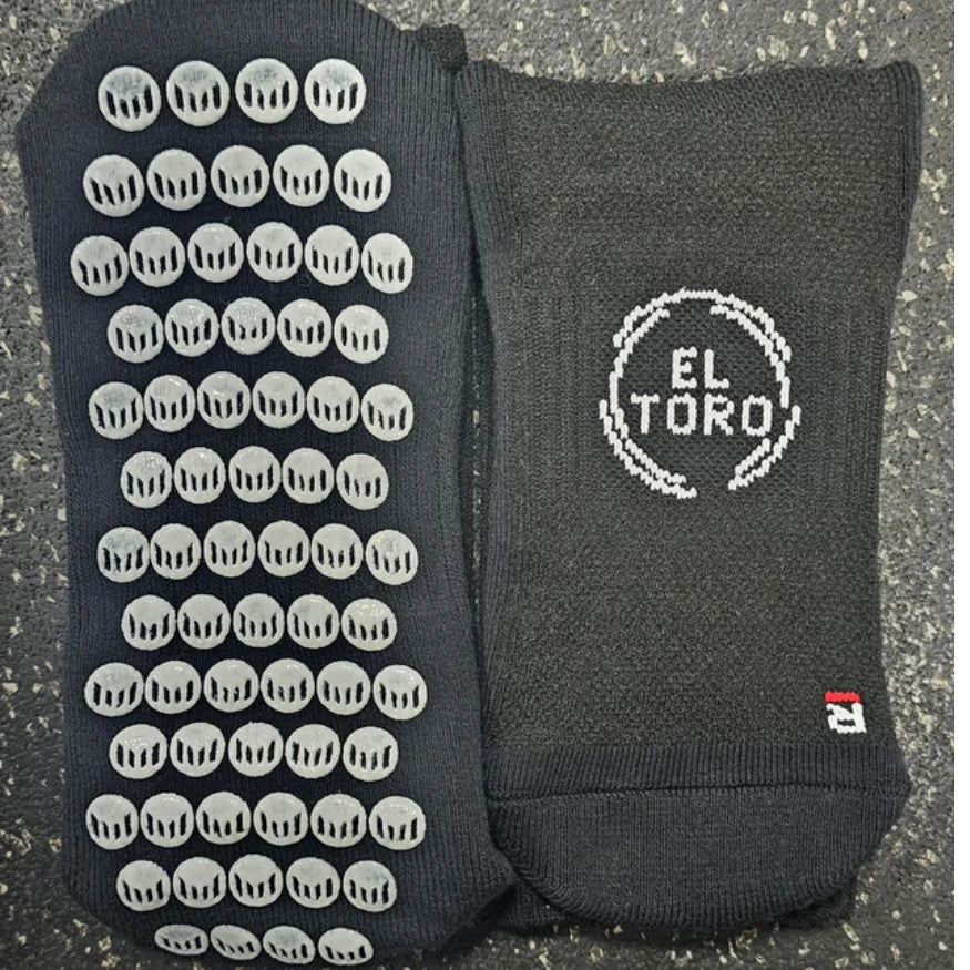 Two pairs of black El Toro grip socks with different patterns on a textured surface