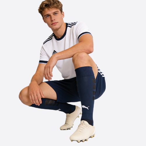 Person wearing a white sports jersey with black accents, navy shorts, and white soccer cleats on a light gray background.