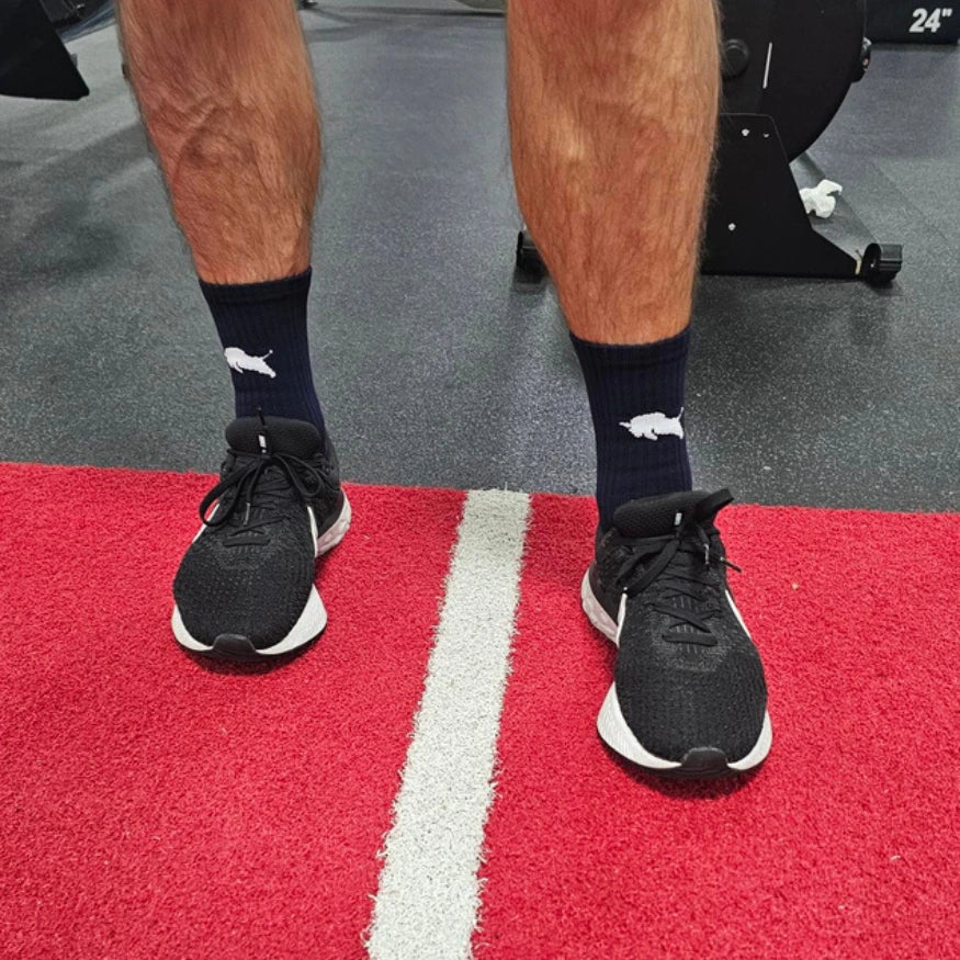 Person wearing black athletic shoes and El Toro grip socks in navy on a red and white striped surface, likely in a gym setting.