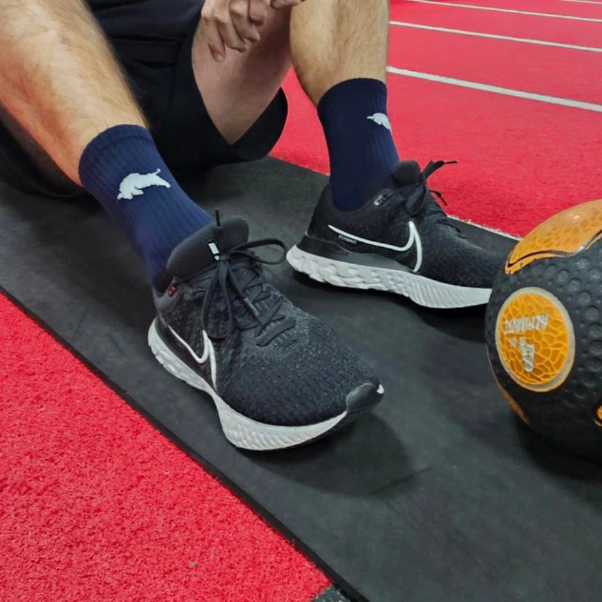 Person wearing navy socks with a white logo and black athletic shoes on a red track.