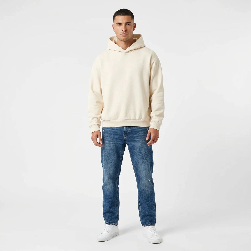 Man wearing a beige hoodie and blue jeans on a white background