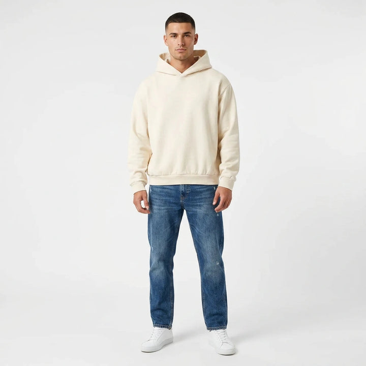 Man wearing a beige hoodie and blue jeans on a white background