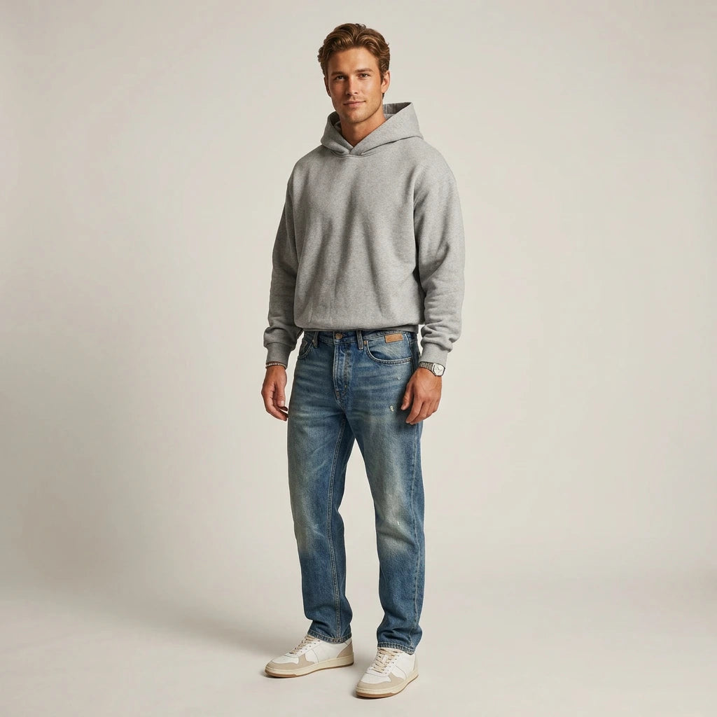 Man wearing a gray hoodie and blue jeans on a plain background