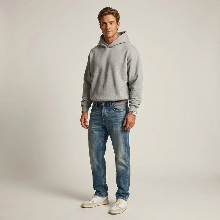 Man wearing a gray hoodie and blue jeans on a plain background