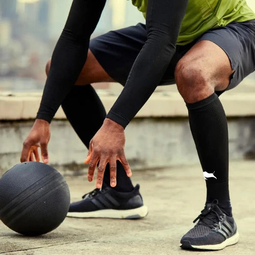 Athlete in sportswear squatting on rooftop, preparing to dribble black basketball wearing Empulse El Toro Black Compression Socks