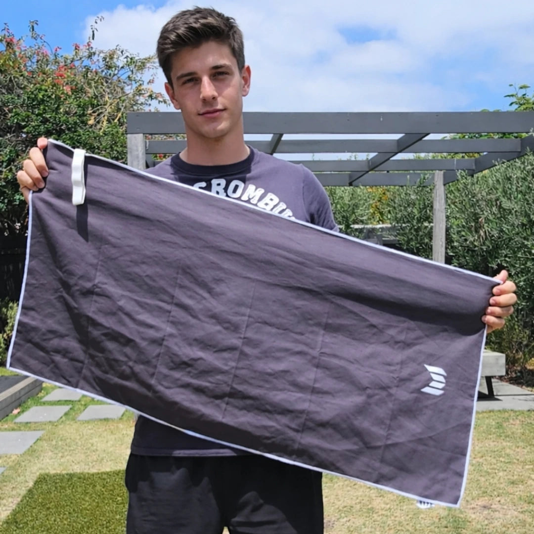 Person holding a large black towel with a brand logo outdoors.