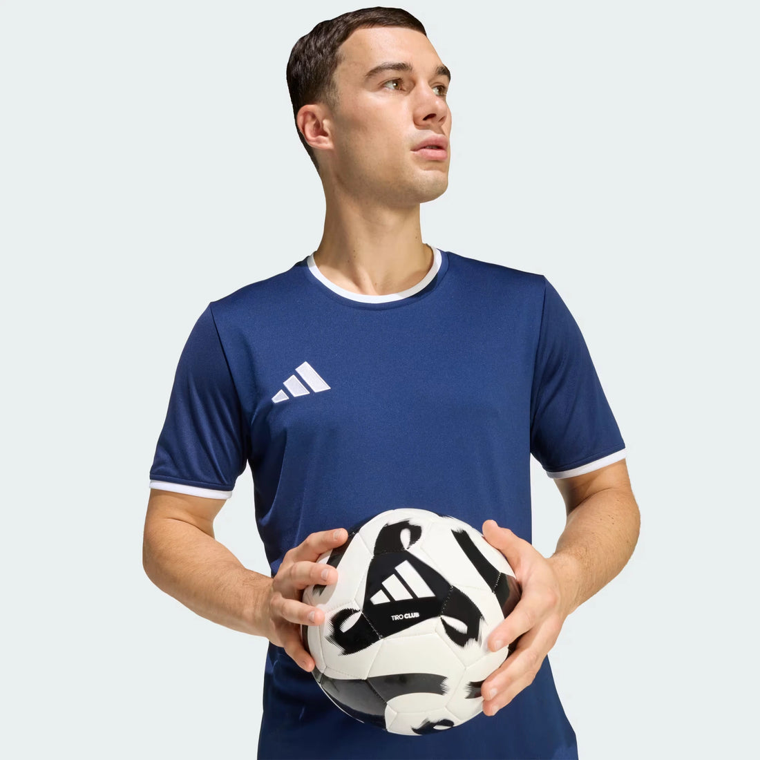 Man holding a soccer ball with an Adidas logo on a light gray background