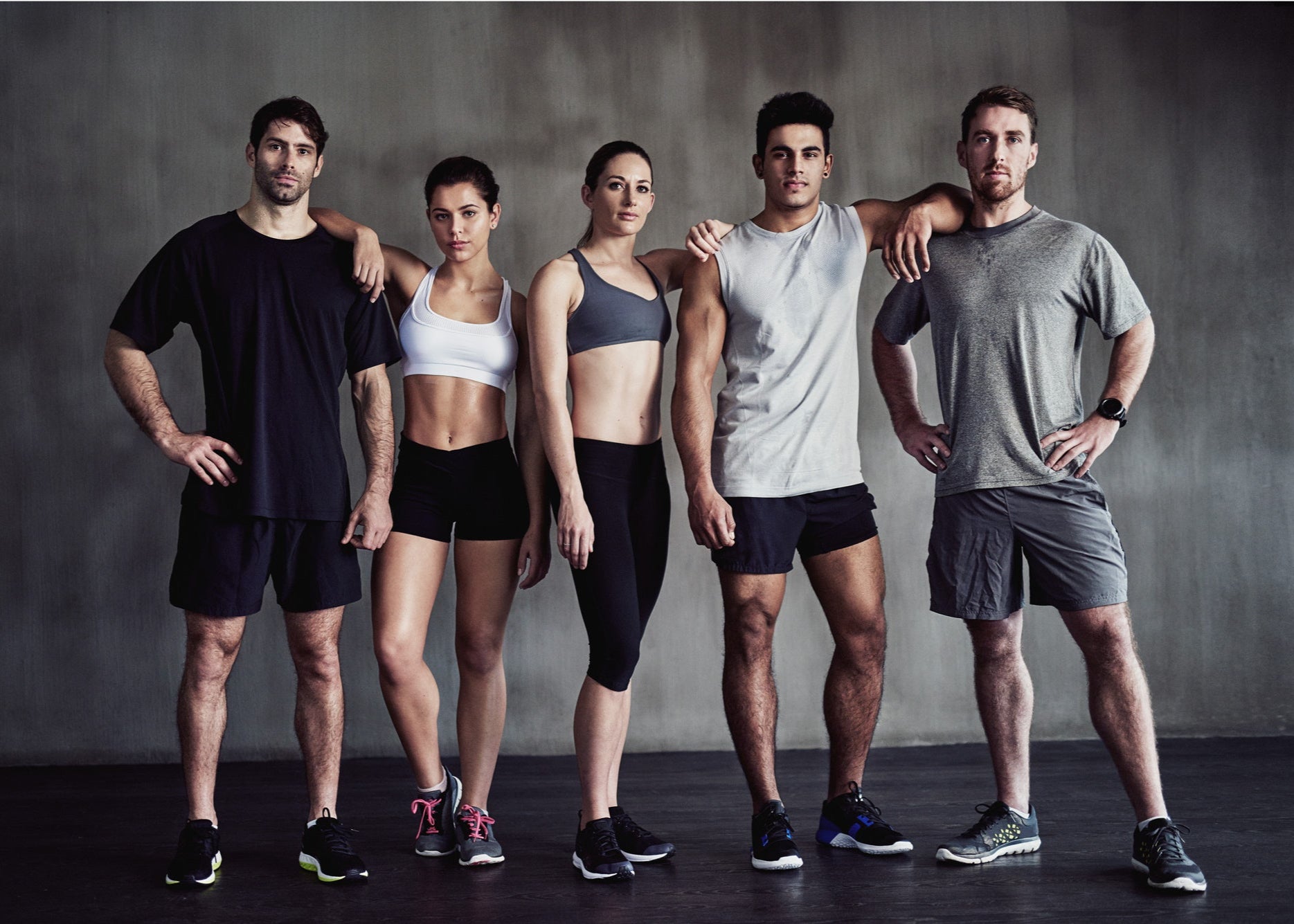 Group of six people in athletic wear posing against a dark background.