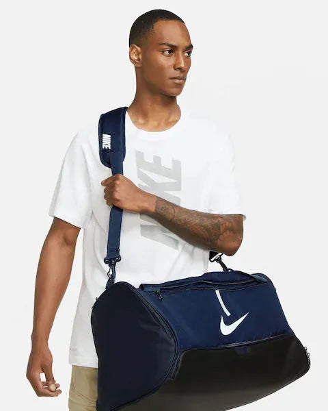 Male model carrying the Nike Brasilia Medium Duffel Bag in navy and black with shoulder strap
