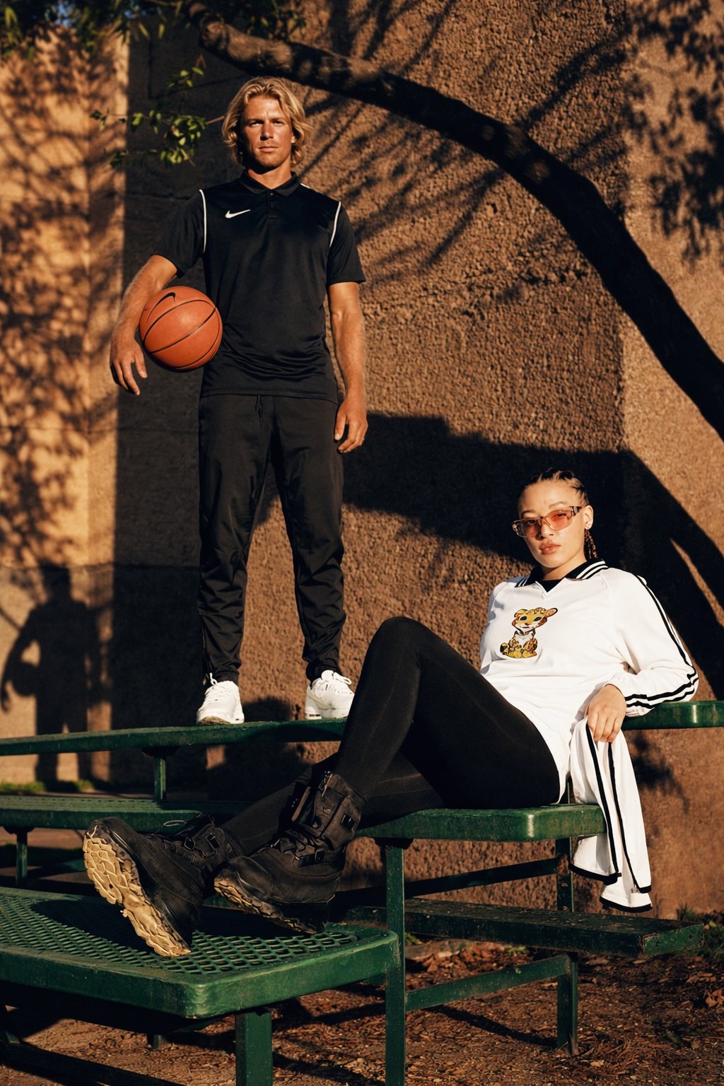 Two people on green benches with one holding a basketball, against a textured wall.