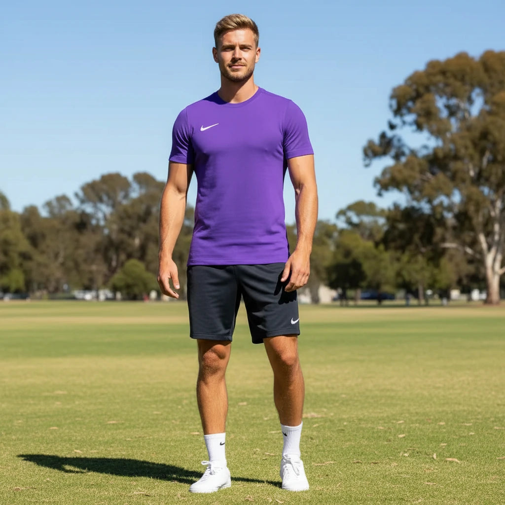 Man wearing a purple Nike shirt and black shorts on a grassy field with trees in the background
