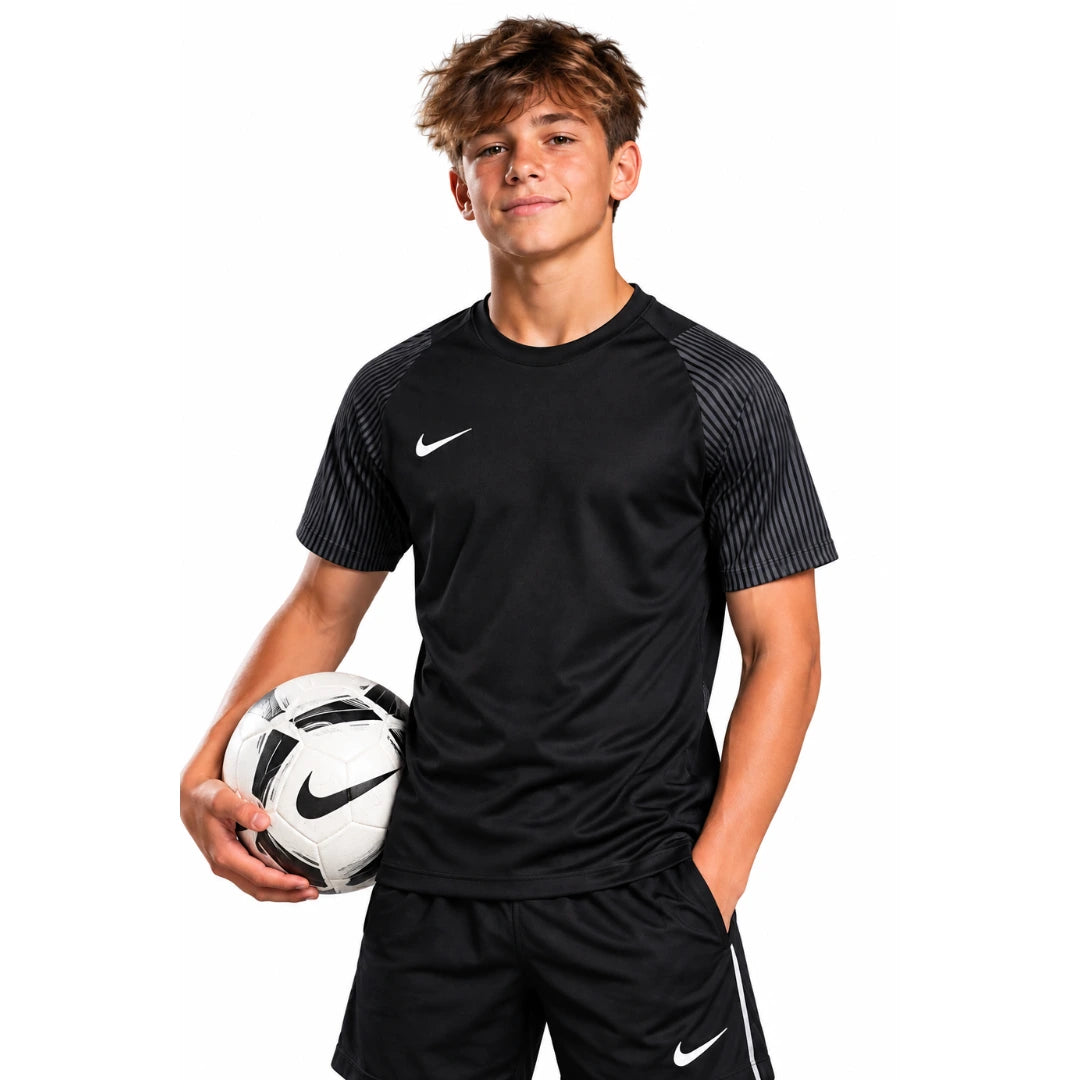 Youth player wearing the black Nike Academy 2 Youth Jersey with patterned grey sleeves, front view, holding a football