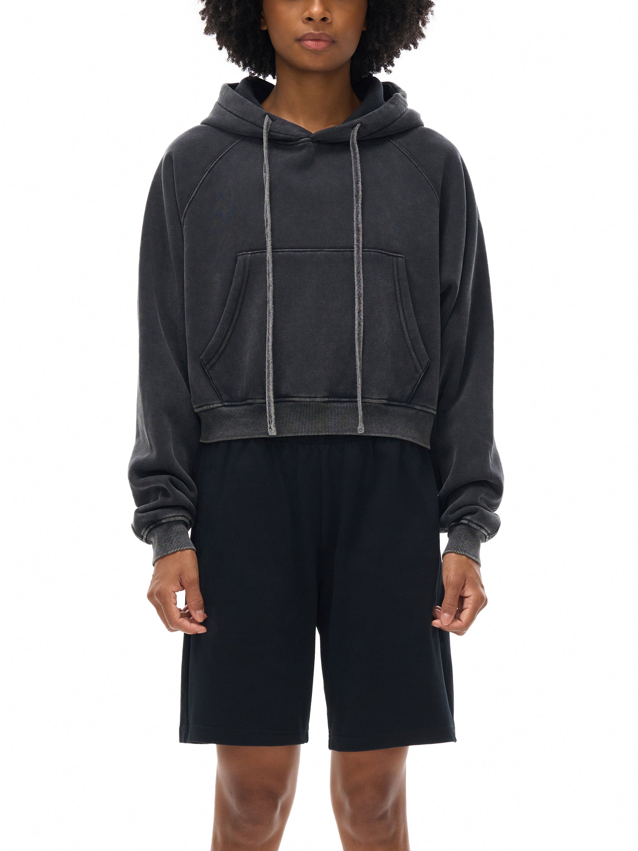 Person wearing a dark gray hoodie and black shorts on a white background