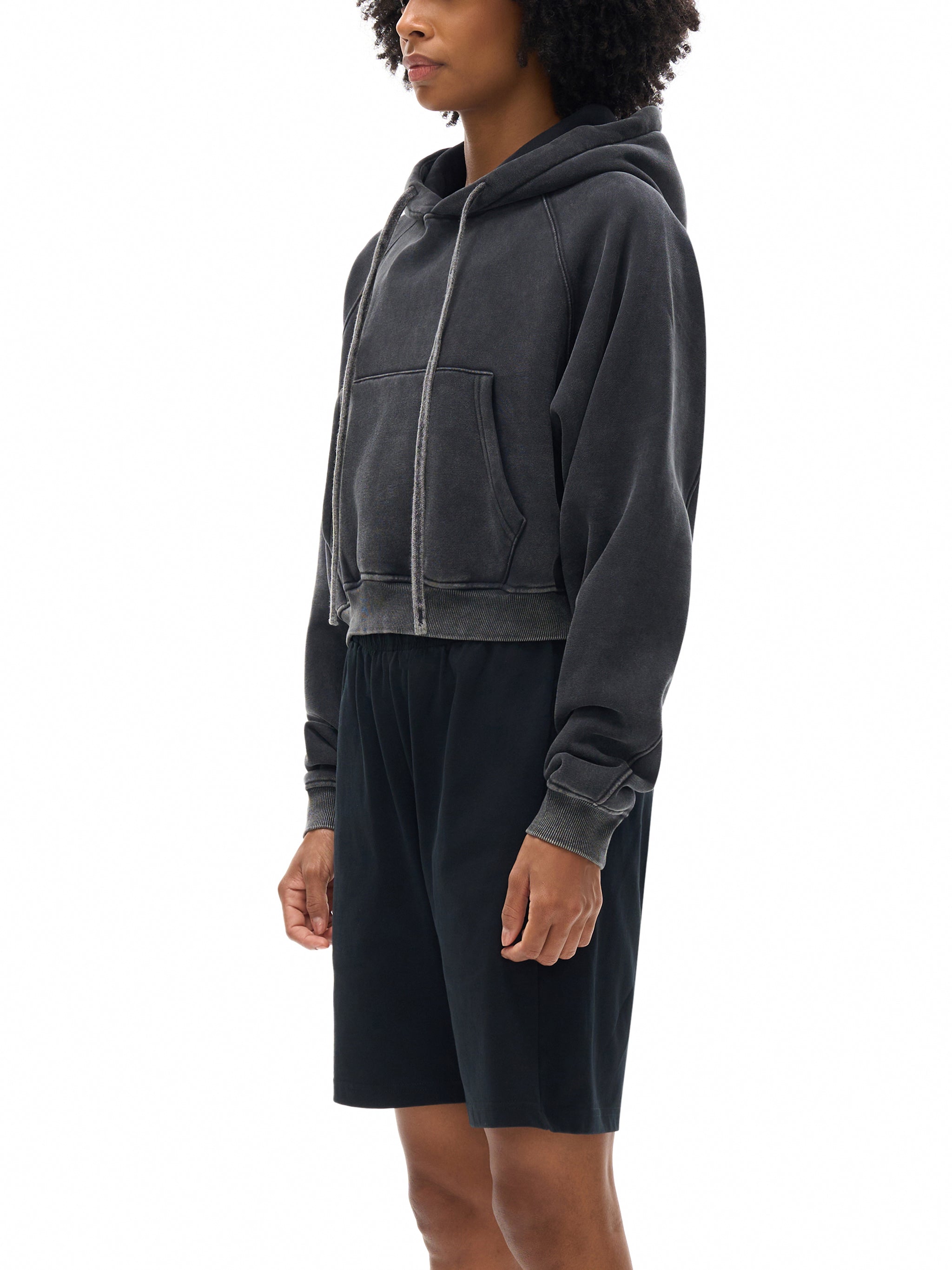 Person wearing a dark gray hoodie and black shorts on a white background