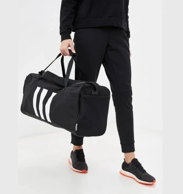Adidas Essentials 3-Stripes Duffel Bag held by model wearing black activewear and sneakers