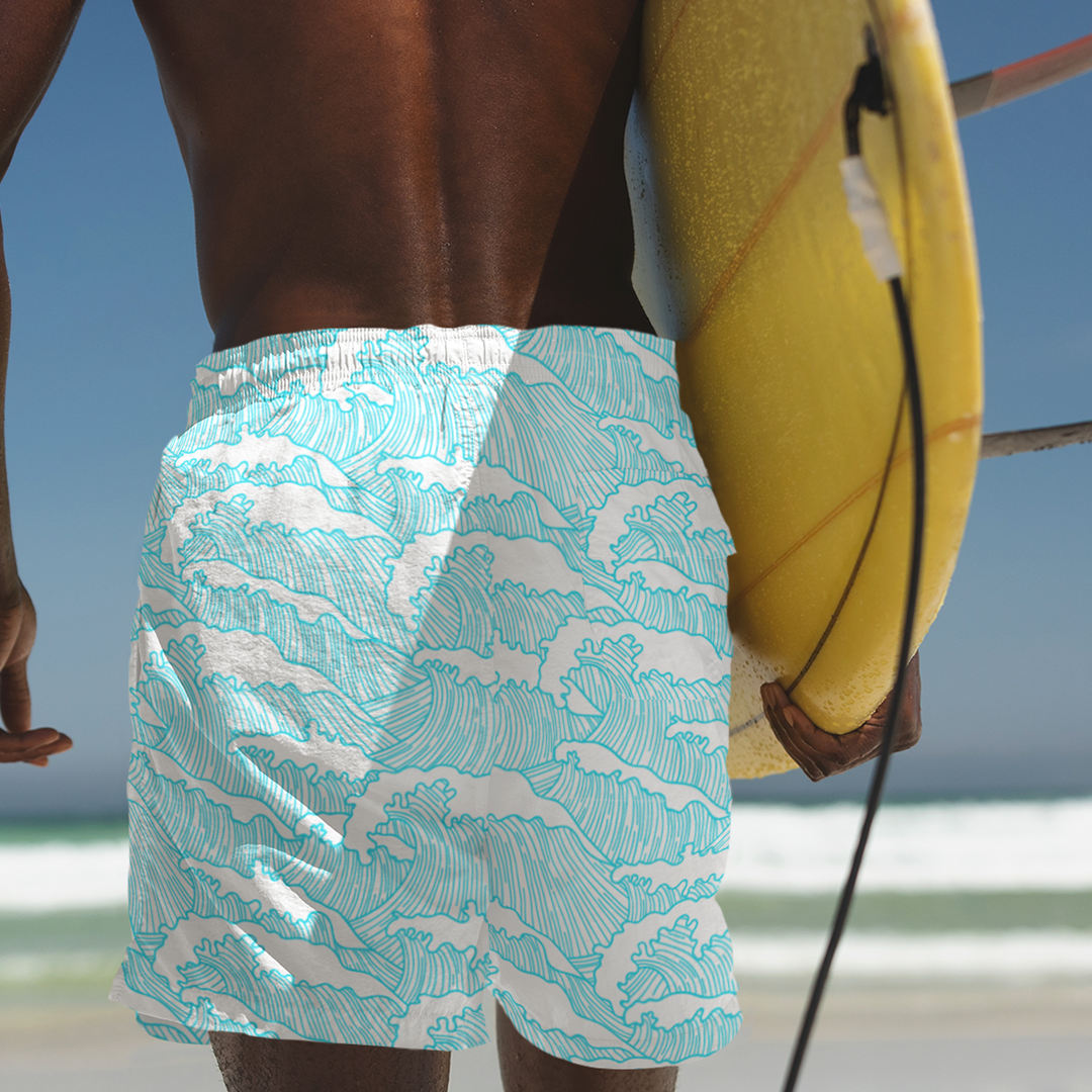 Rear view of Empulse™ Aqua Tides swim shorts next to surfboard at the beach