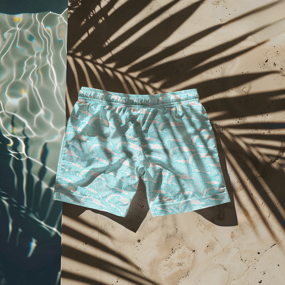 Flat lay of Empulse™ Aqua Tides shorts under palm shadows on light sand