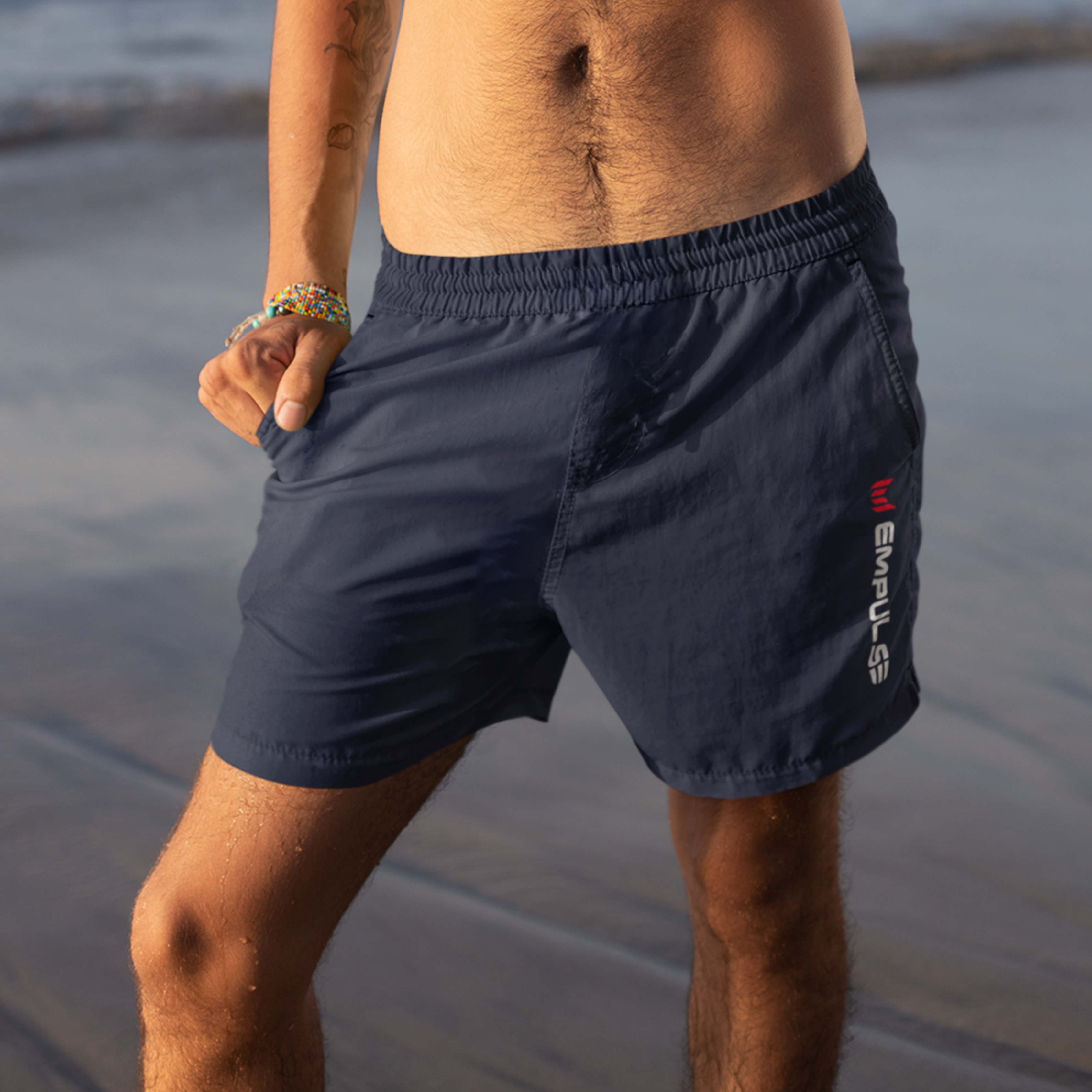 Empulse™ Blue men’s swim shorts worn at shoreline with logo in clear view