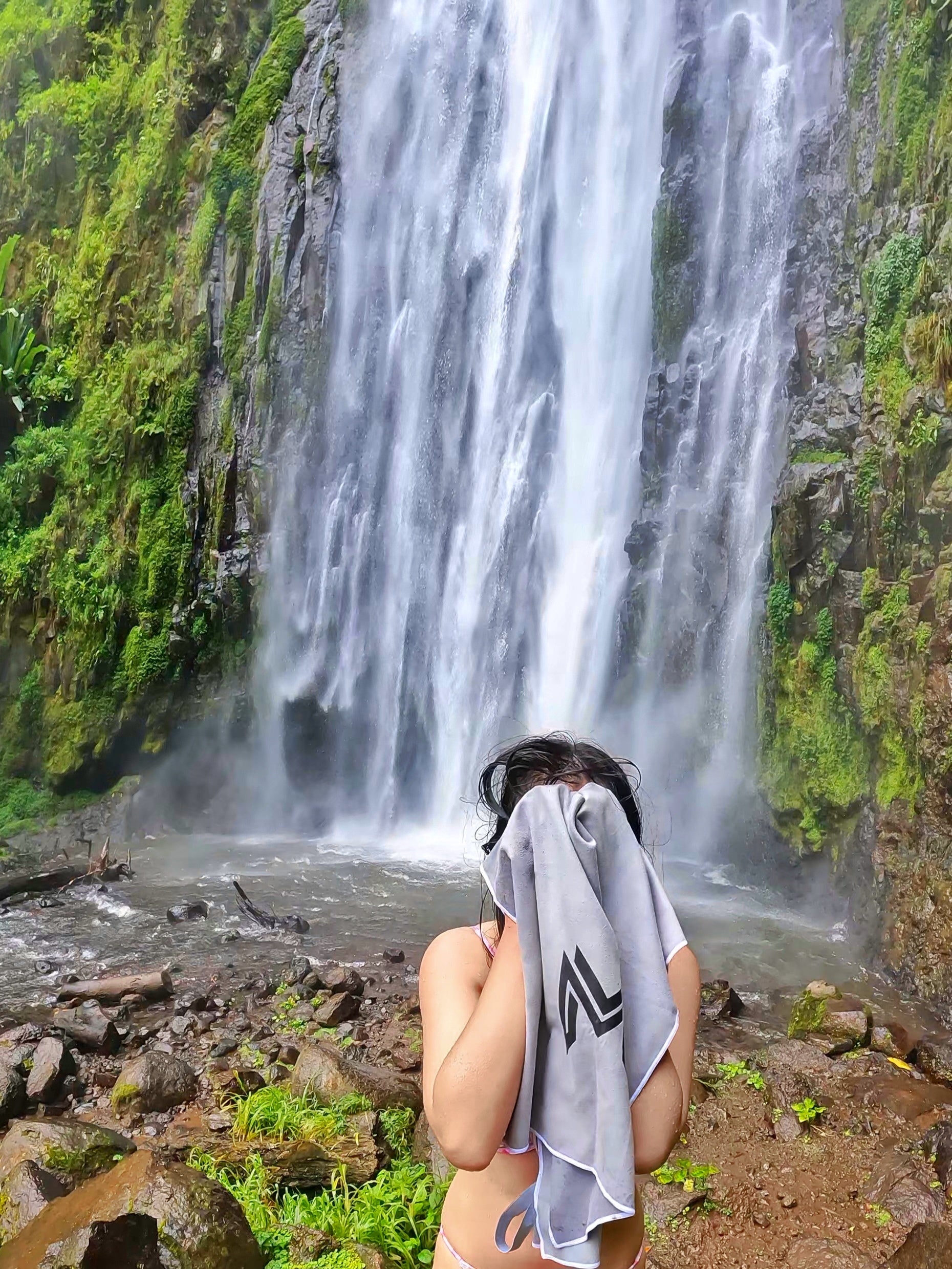 Flat lay of Empulse™ Carbon Cool towel placed on rocks near natural waterfall setting