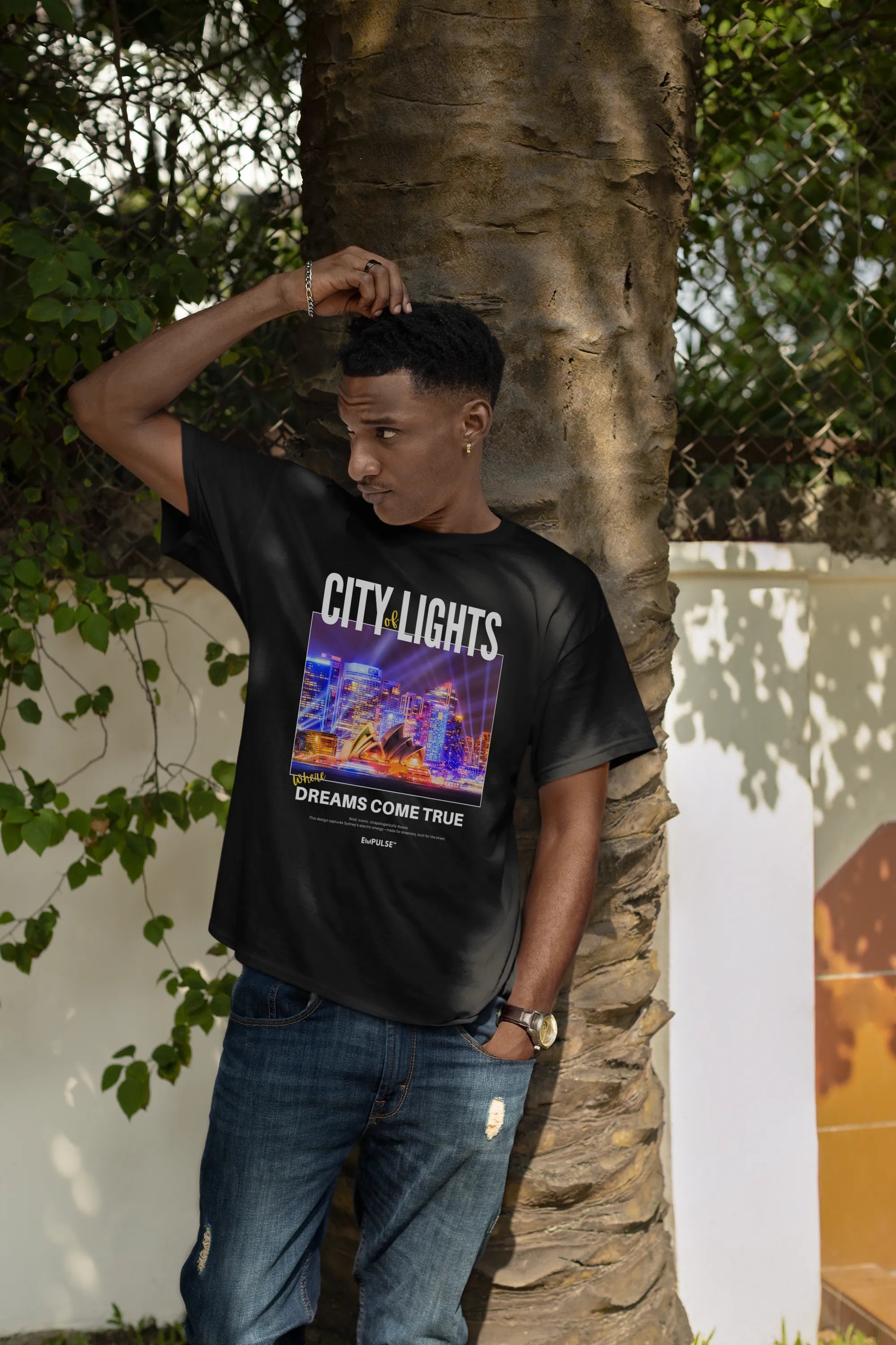 Man posing near a tree in Empulse™ black City Lights tee, featuring bold street-style Sydney skyline design