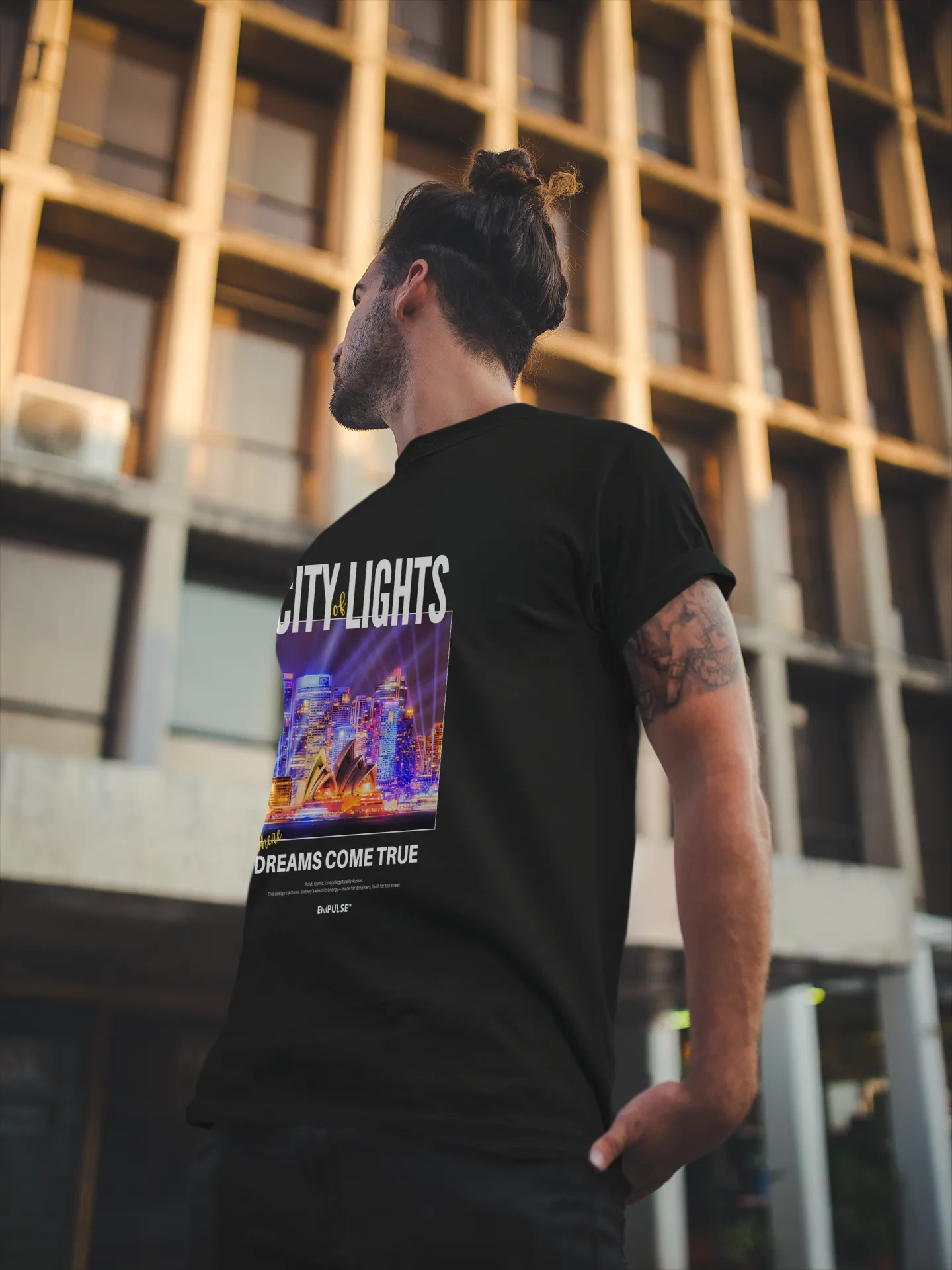 Back view of man in Empulse™ black City Lights tshirt standing against an urban building facade in natural light


