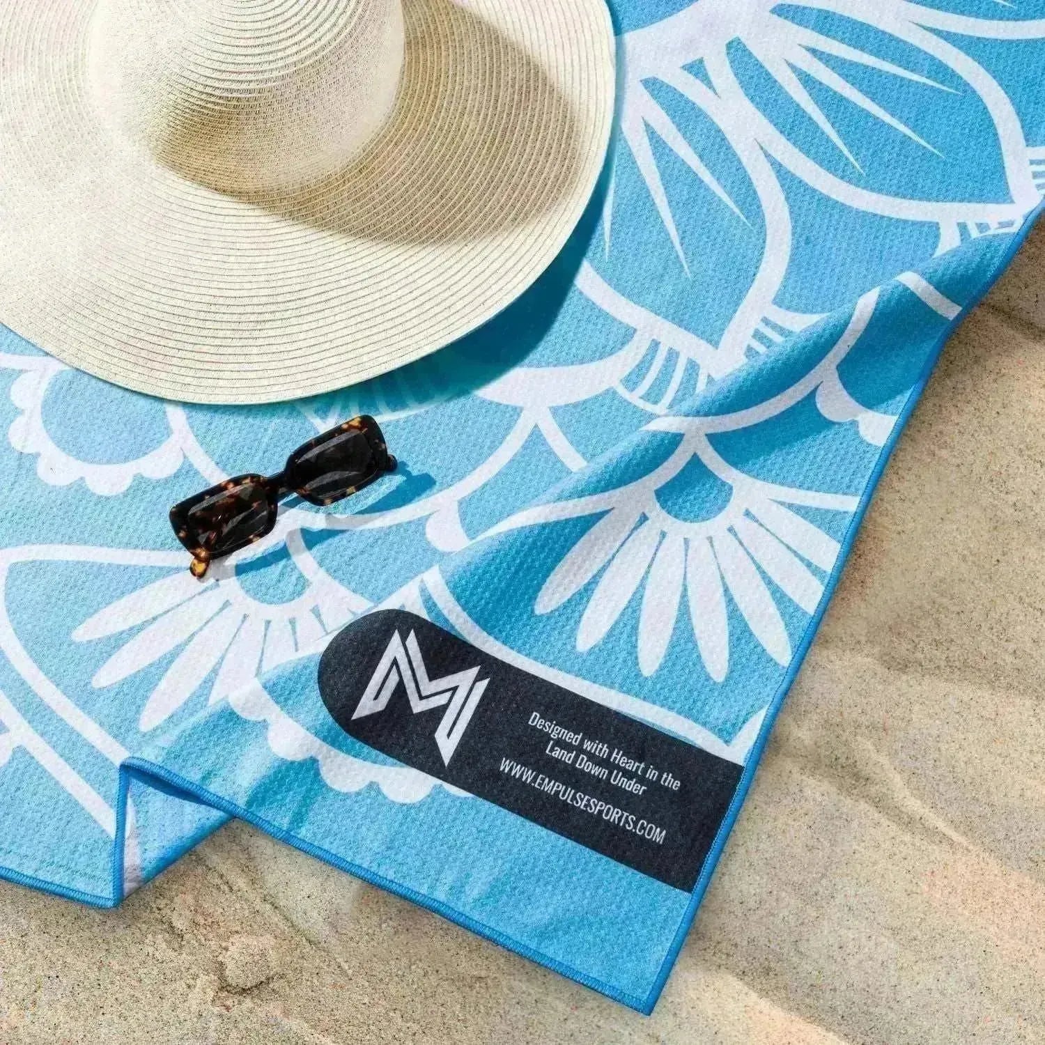 Empulse™ Coastal Chill towel laid on sand with sunglasses