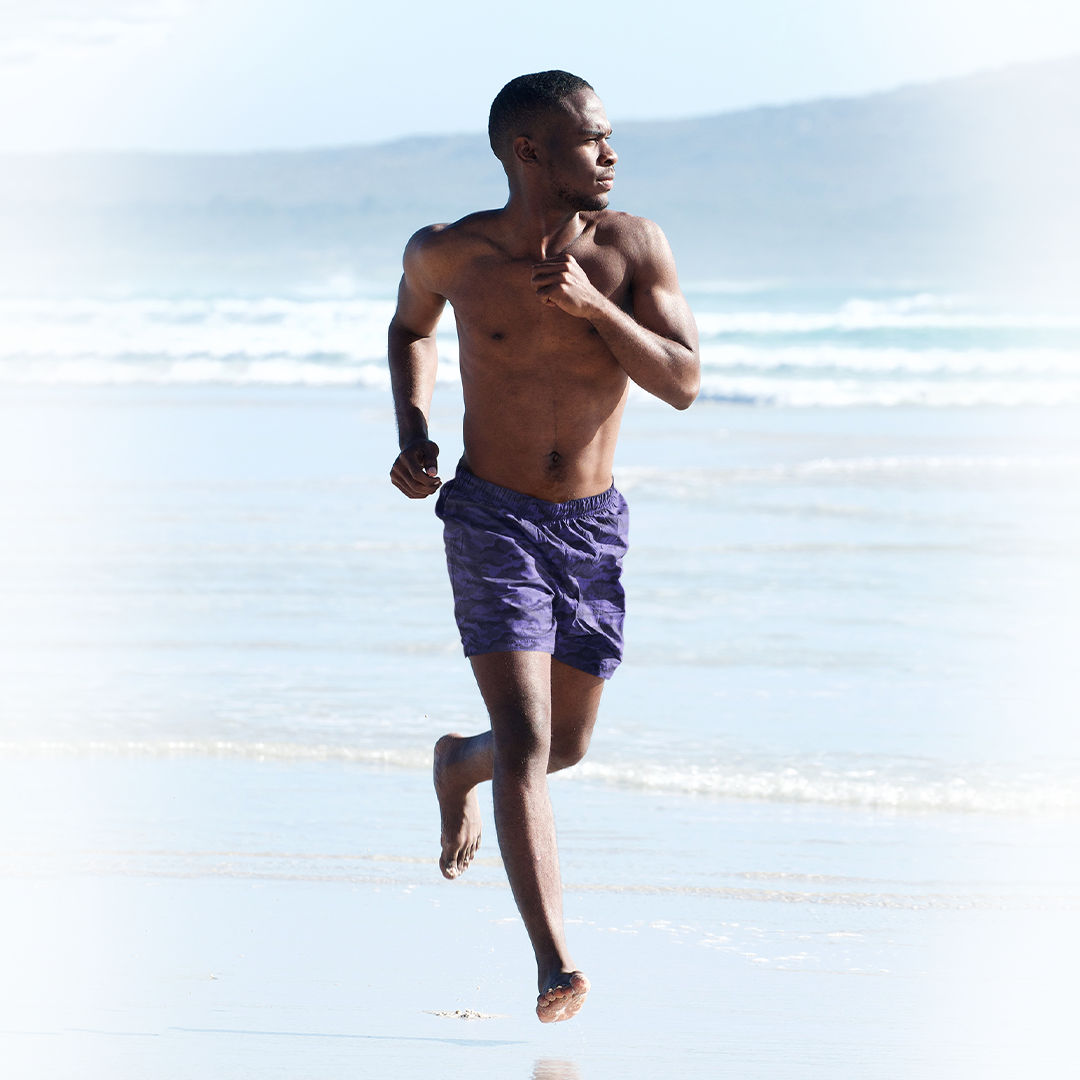 Male model wearing Empulse™ Cobalt Camouflage swim shorts running on beach toward ocean