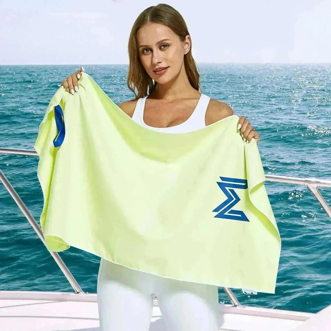 Female model holding full Empulse™ Lemon Zest towel open by the ocean with breeze in background