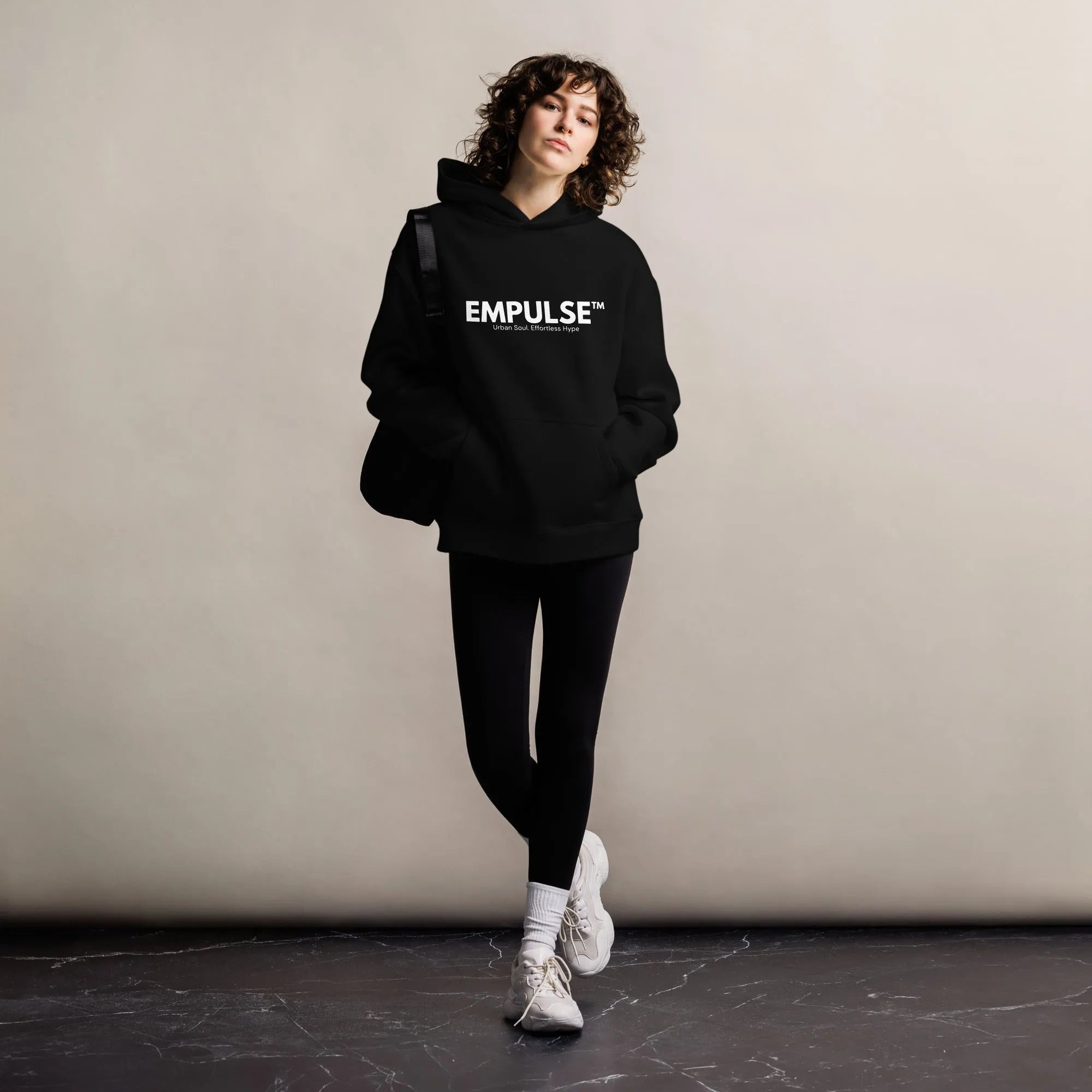 Woman wearing Empulse™ logo hoodie leaning casually against indoor wall with clean, urban vibe