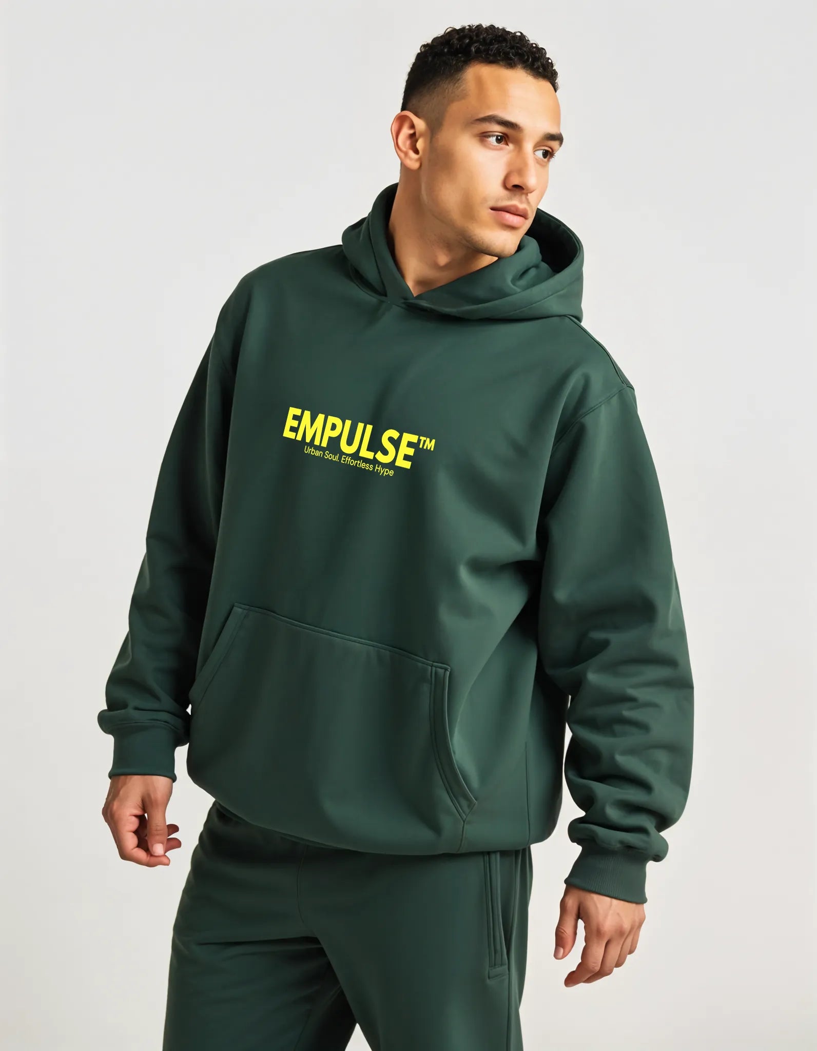 Side view of man wearing Empulse™ forest green hoodie, casual pose in modern studio