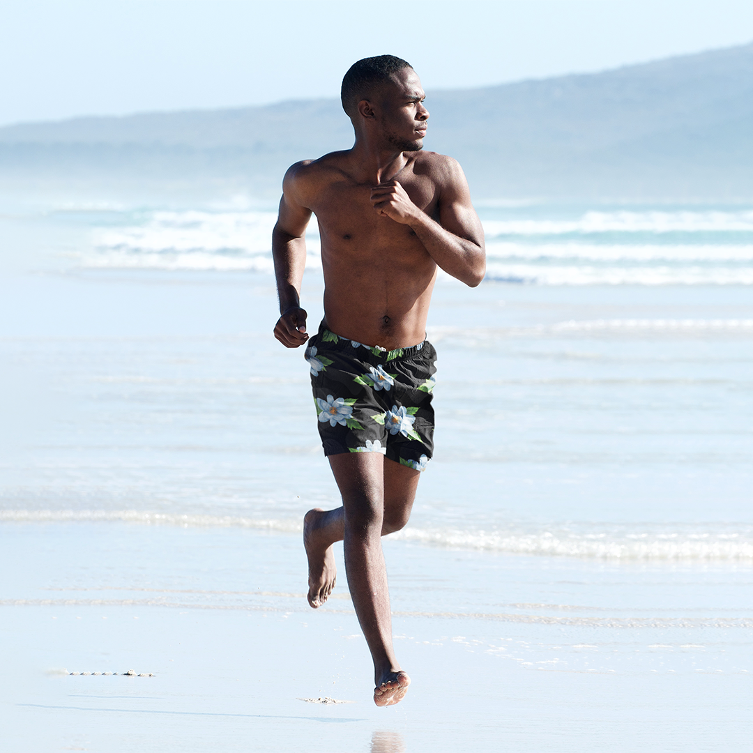 Male model running along shoreline in Empulse™ Orchids shorts with black floral pattern