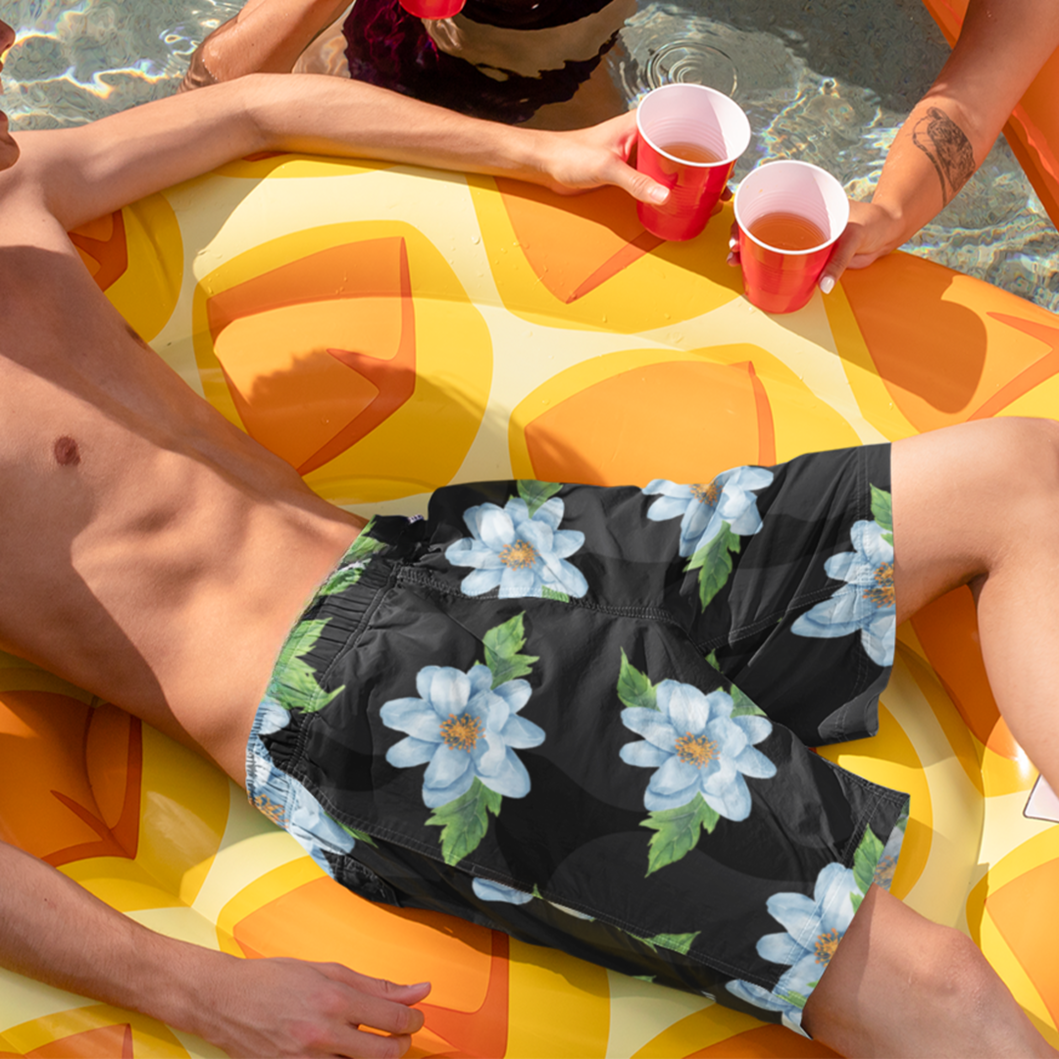 Model lounging on inflatable wearing Empulse™ Orchids swim shorts with floral print