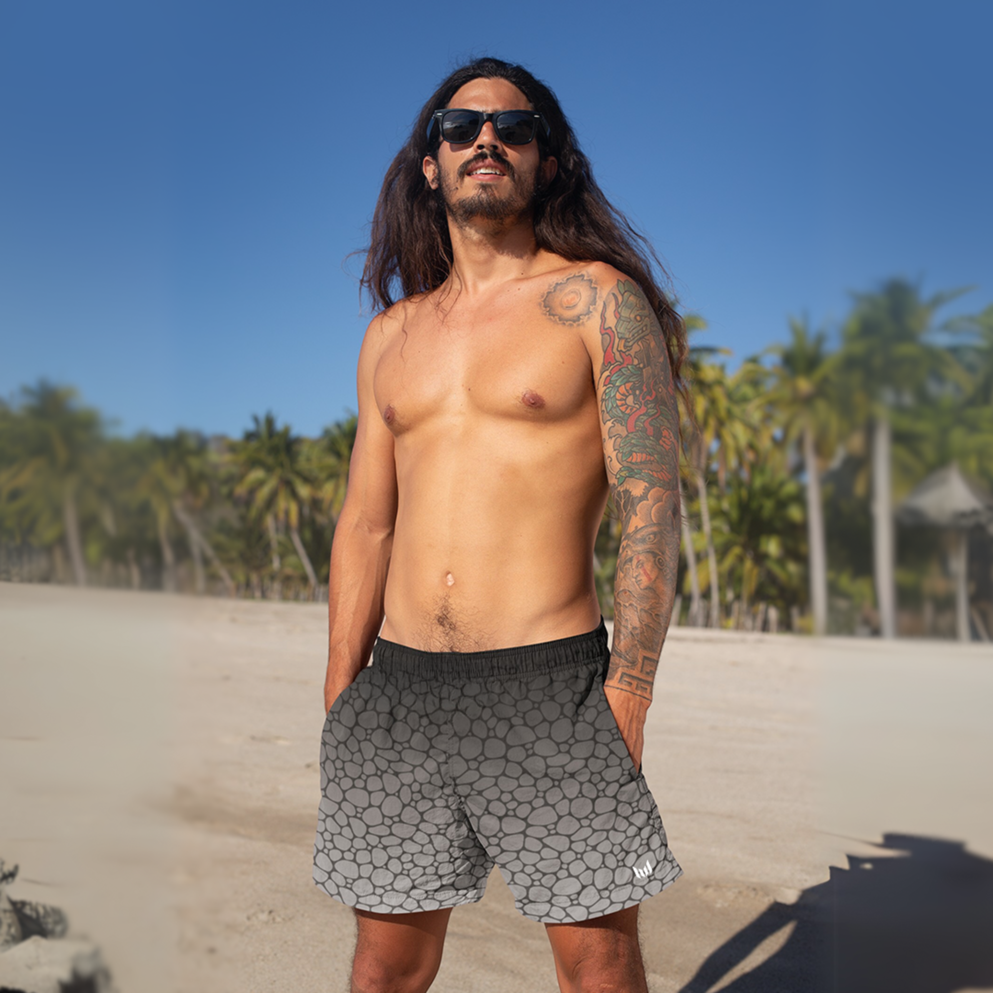 Empulse™ Pebbles swim shorts worn by model on tropical beach with palm trees