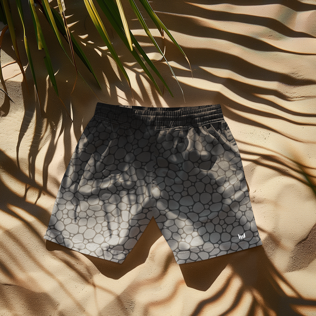 Empulse™ Pebbles swim shorts laid on white towel with palm shadows