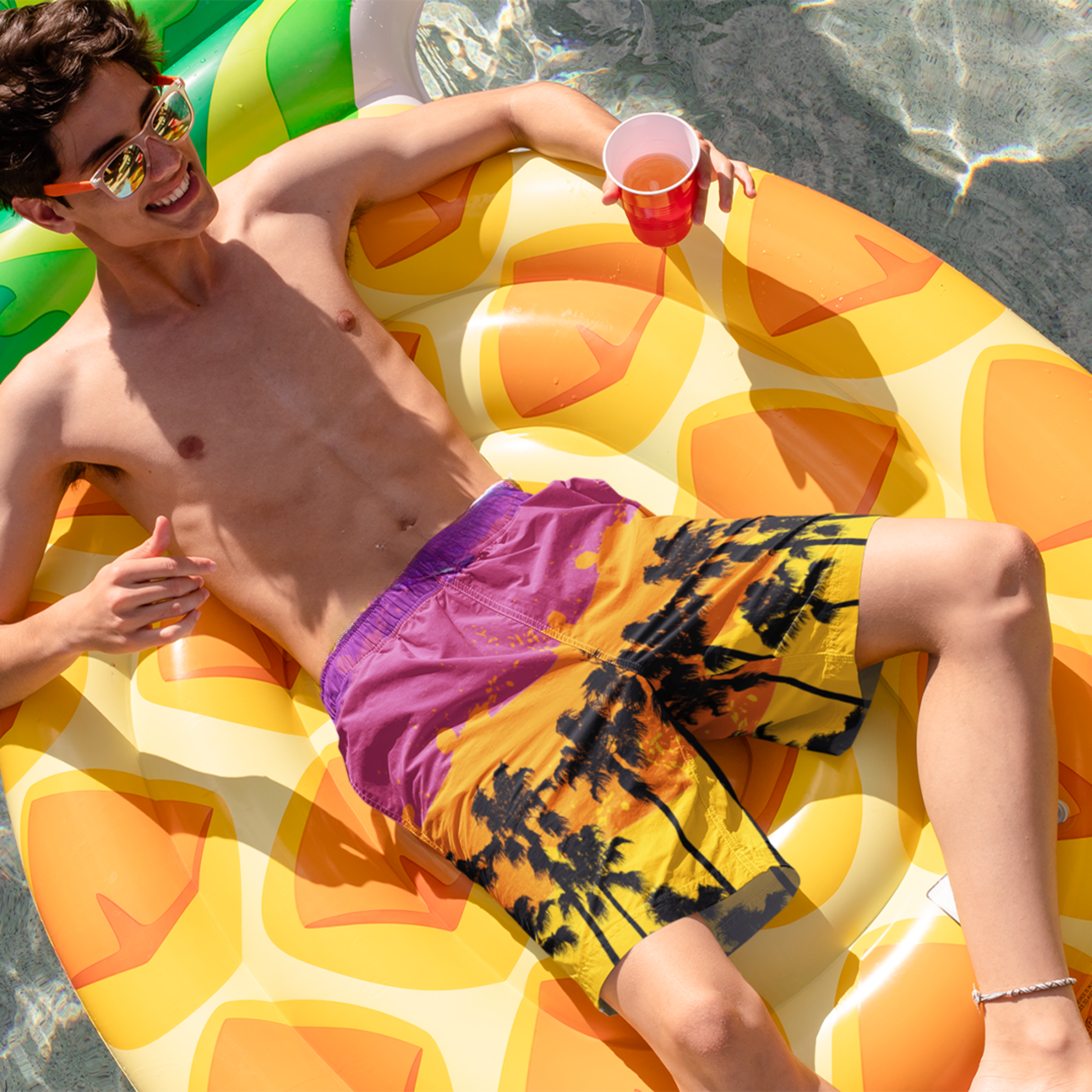 Model floating in pool wearing Empulse™ Tropical shorts with bright orange-pink sunset tones