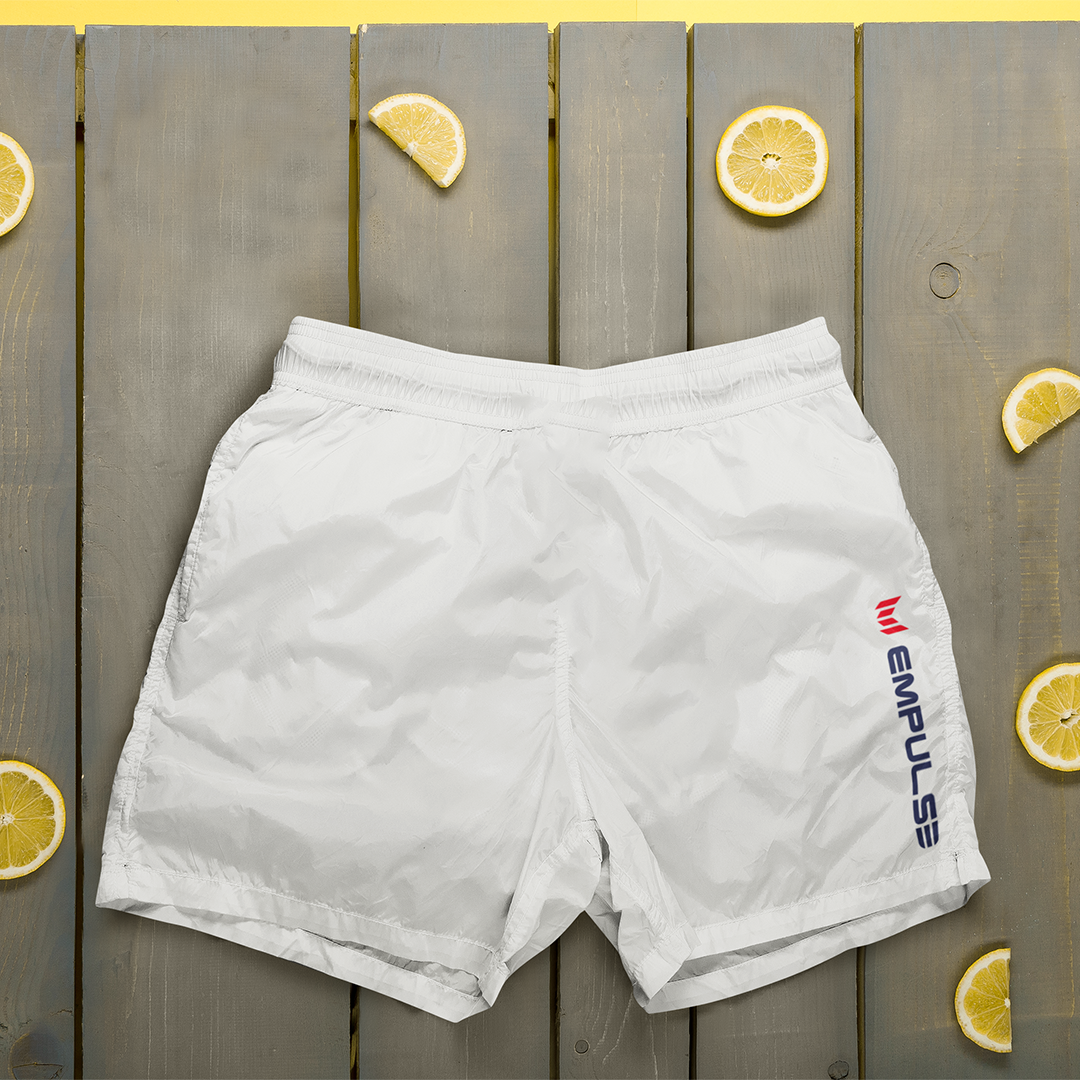 Flat lay of Empulse™ White swim shorts with coins on a wooden deck background


