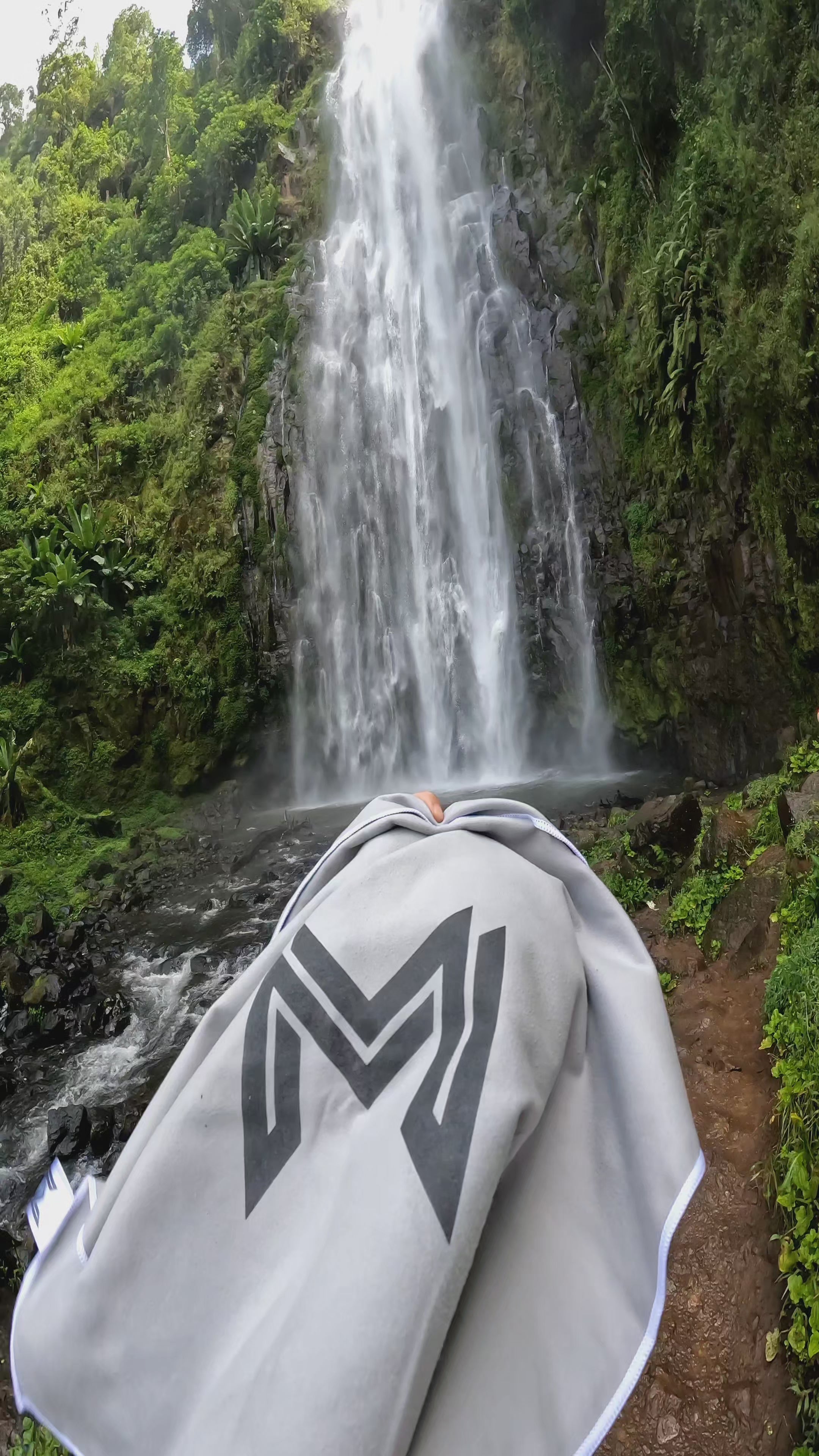 Model using Empulse™ Carbon Cool towel while hiking near scenic waterfall