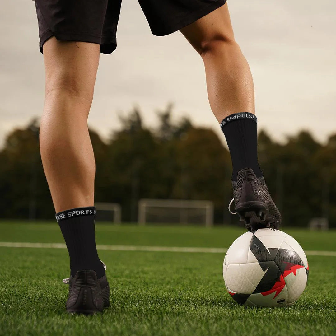 Athlete lacing boots while wearing black compression socks on grass field with soccer boots with a soccer ball