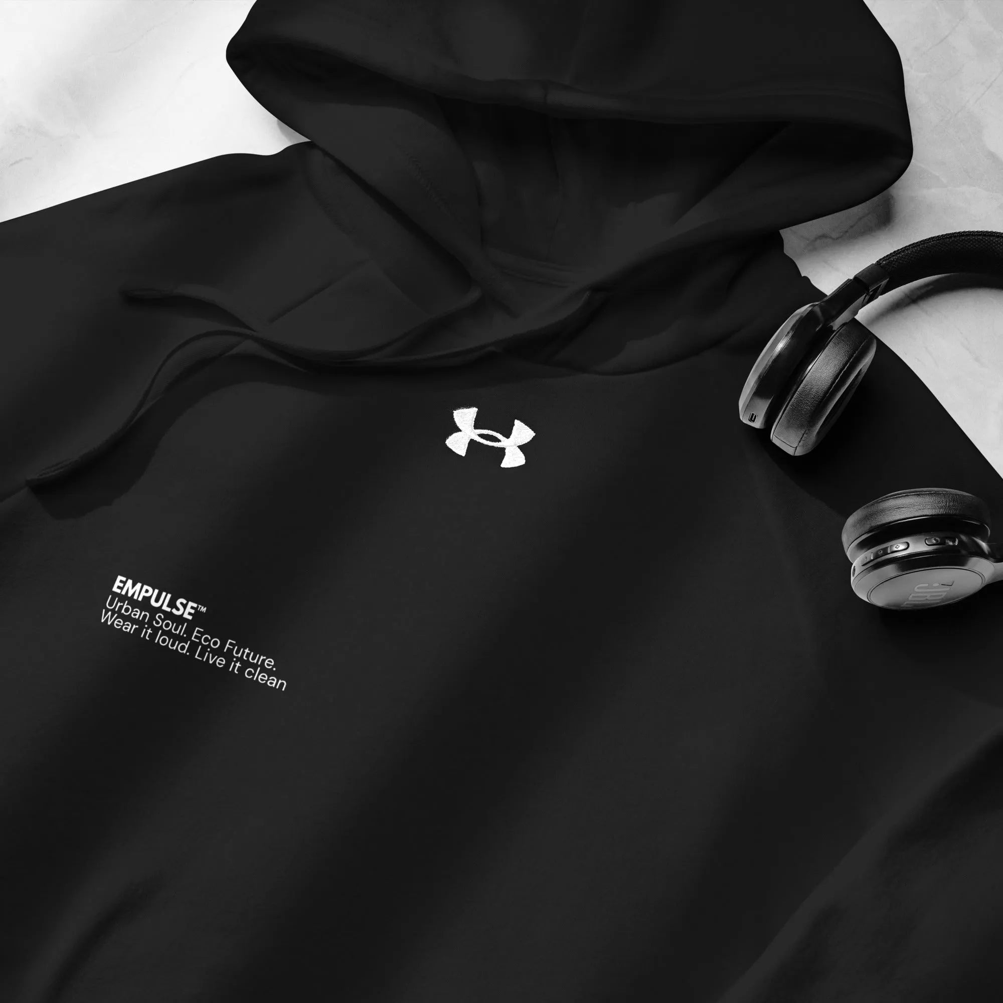 Flat lay of Under Armour black hoodie showing logo and pocket with headphones